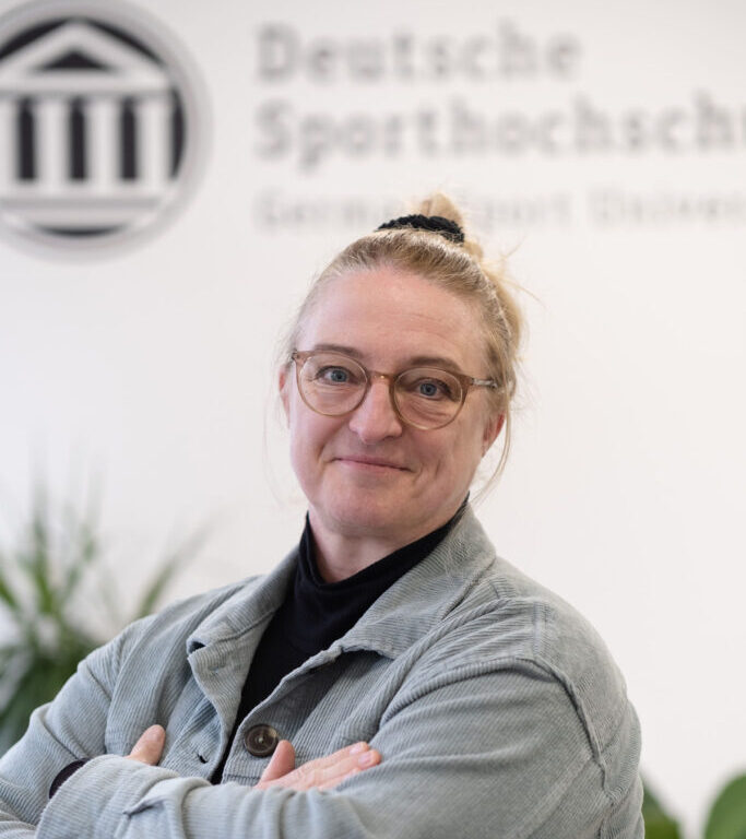 Das Foto zeigt Marion Sulprizio. Sie blickt in die Kamera. Hinter ihr an der Wand sieht man das Logo der Deutschen Sporthilfe.