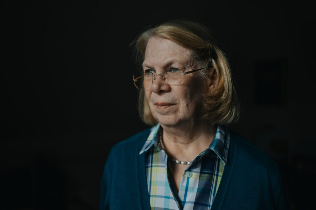 Ein Foto von Ingrid Liebs. Sie trägt eine Brille, kariertes Hemd und eine dunkelblaue Strickjacke.