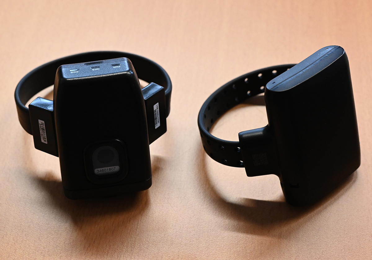 Zwei elektronische Fußfesseln liegen auf einem braunen Boden. Fußfessel nach spanischem Modell