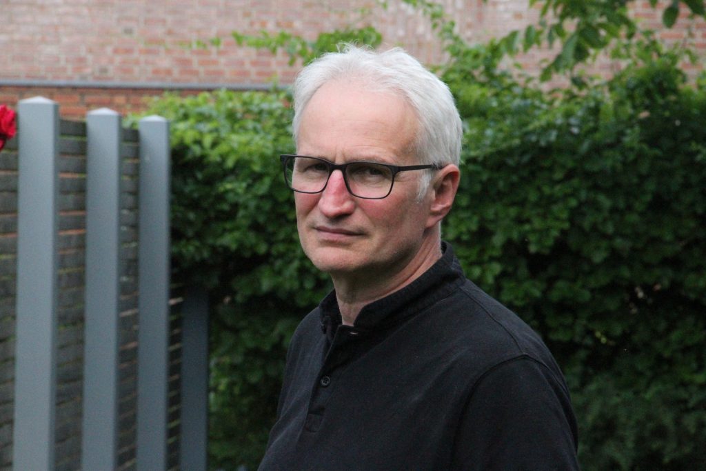 Ein Mann mit Brille steht in einem Garten und schaut in die Kamera.