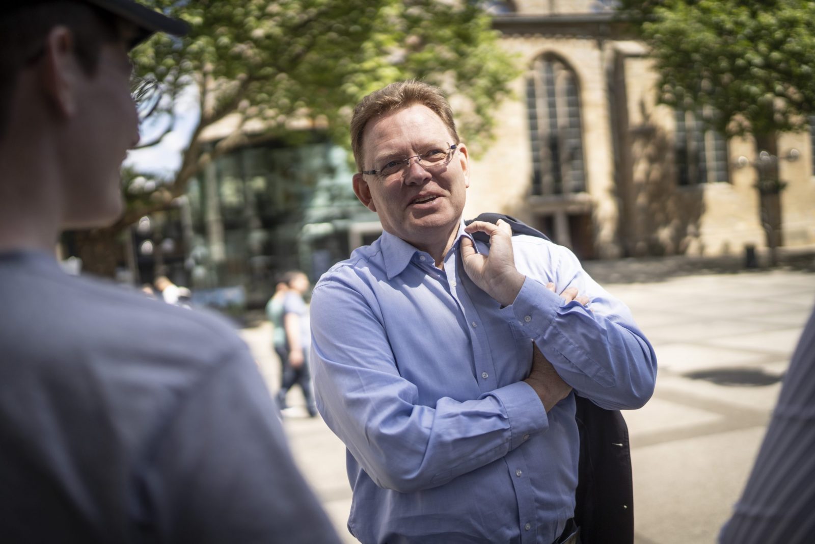 Ein Mann mit Brille hält ein Sakko über der Schulter.